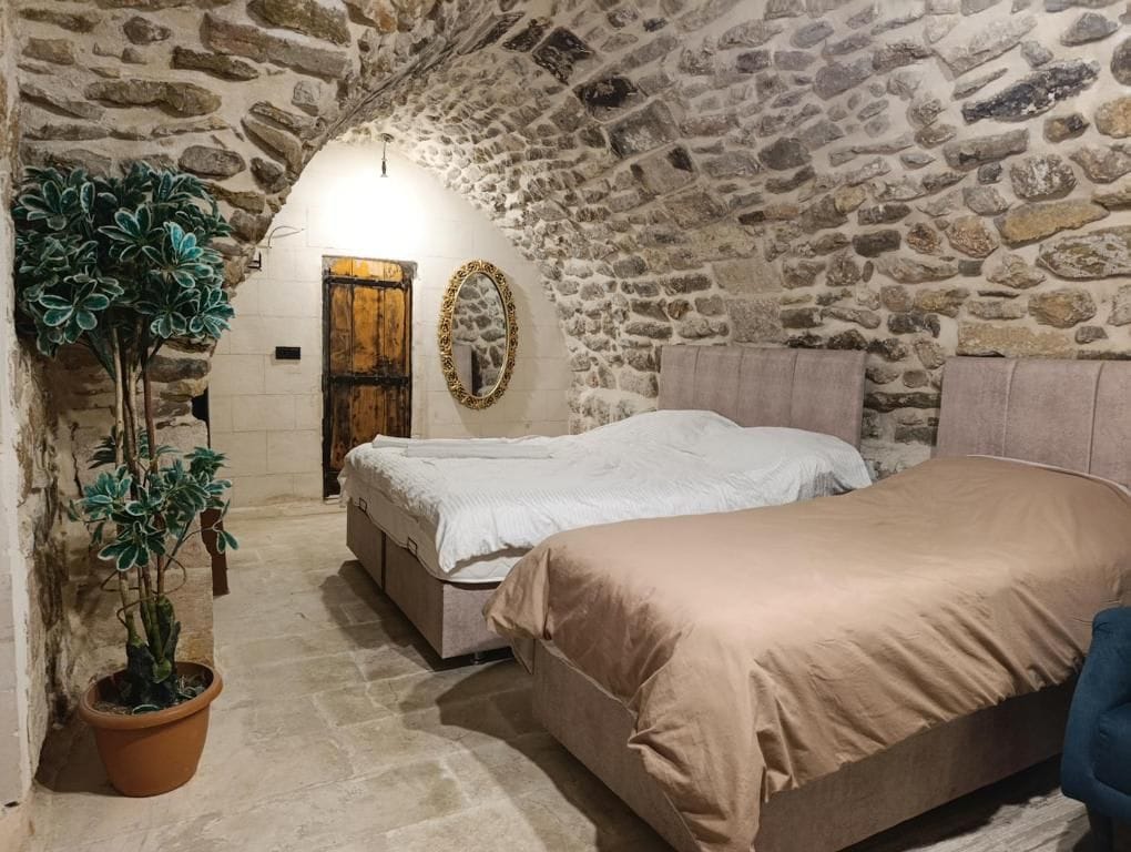 Una habitació amb parets de pedra, un llit, una panxa i una planta en test.