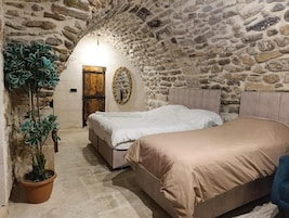 Una habitación con paredes de piedra, una cama, un banco y una planta en maceta.