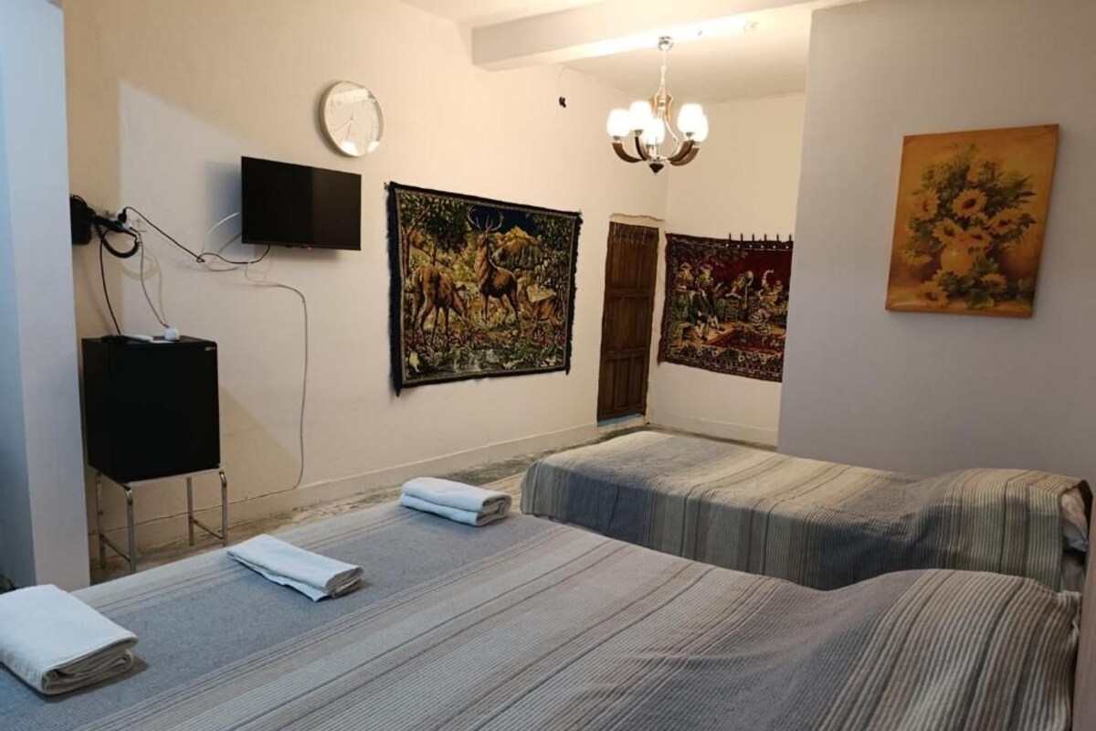 Hotellihuone, jossa on kaksi sänkyä, taulutelevisio, taideteoksia seinillä ja kattokruunu.