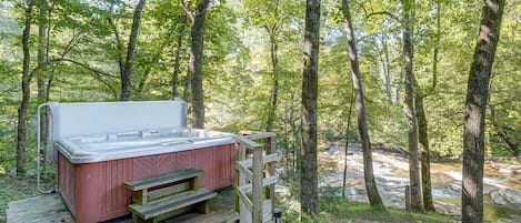 A hot tub in a forested area with a wooden deck and steps leading up to it.