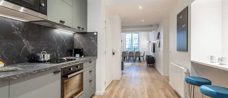 A modern kitchen with a marble countertop, built-in oven, and a dining area with a table and chairs.