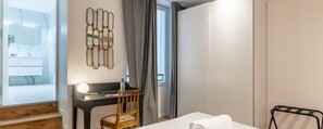 Ein Hotelzimmer mit Bett, Schreibtisch mit Stuhl, Spiegel, Wandbild und Blick ins Badezimmer.