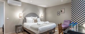 Ein Hotelzimmer mit Bett, Nachttischlampen, einem Sessel, einem Schreibtisch mit Wasserflaschen und einer gestreiften Wand.