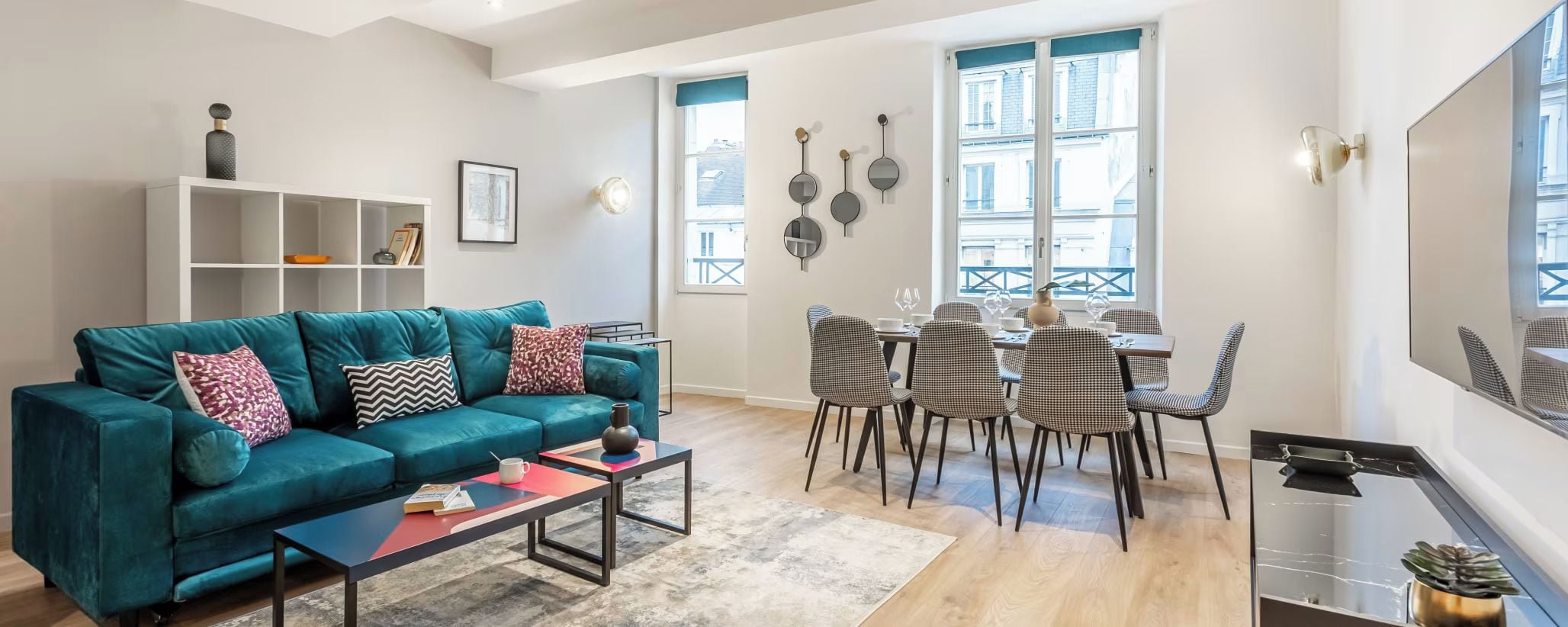 A living room with a teal sofa, a coffee table, and a dining area with checkered chairs and a table.
