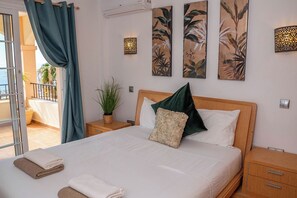 Ein Hotelzimmer mit Bett, Nachttisch, Blumentopf und Blick ins Freie.