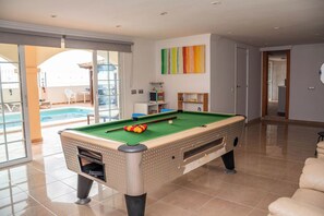 Ein Billardtisch in einem Raum mit Blick auf ein Schwimmbecken, eine Tür zu einem anderen Raum und ein farbenfrohes abstraktes Gemälde an der Wand.