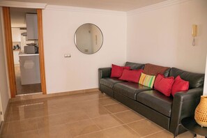 A living room with a leather sofa, a round mirror, and a kitchen visible through an open door. - Spanish Villa with Hot tub/pool amazing views. (Adeje)