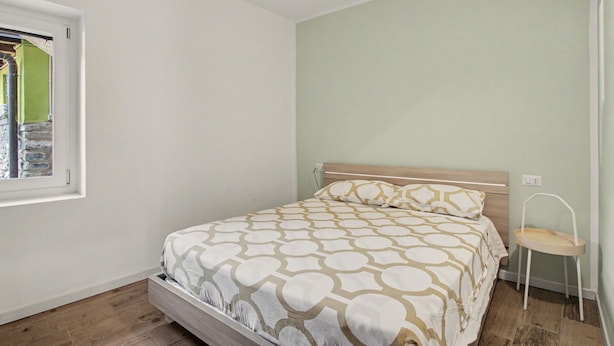 Un dormitorio con cama, ventana, silla y toma de corriente.