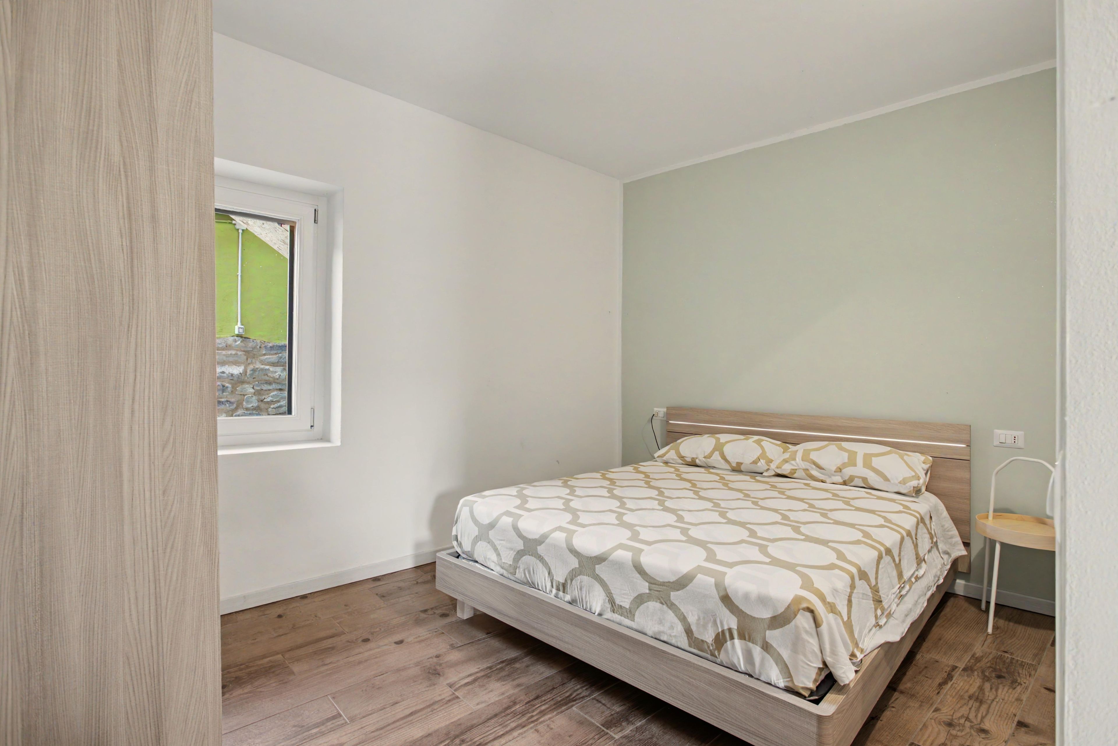 A bedroom with a single bed, a window, and a wooden floor.