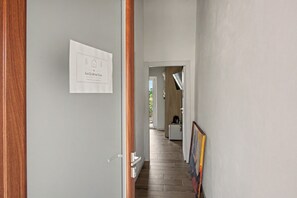 Un pasillo con una puerta a la izquierda, un cartel enmarcado en la pared y una zona de cocina al fondo.