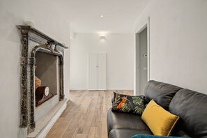 Una habitación con chimenea, un sofá con cojines y suelo de madera.