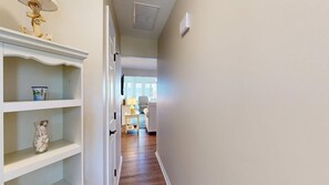 Un pasillo con estantes blancos, un jarrón y una puerta que da a una habitación con una silla y una lámpara.