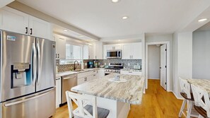 A modern kitchen with stainless steel appliances, a marble island, and white cabinetry. - Keen-Wik on the Bay - 38351 Walnut Ln (Selbyville)