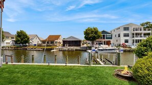 A waterfront property with a dock, a grassy lawn, and a building with a covered patio. - Keen-Wik on the Bay - 38351 Walnut Ln (Selbyville)