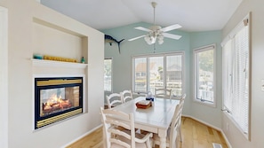 A dining area with a fireplace, white chairs, a table, and a ceiling fan. - Keen-Wik on the Bay - 38351 Walnut Ln (Selbyville)