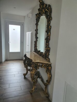Una habitación con un espejo grande y ornamentado, suelo de madera y una puerta blanca.