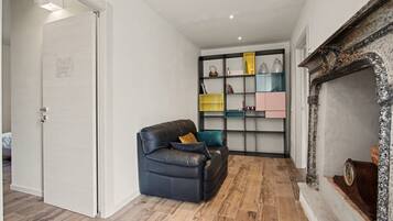 Een woonkamer met een zwarte leren bank, een houten vloer en een open haard met decoratieve boekenplank.
