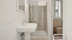 Un baño con un lavamanos blanco, una ducha con azulejos estampados y una puerta que da a otra habitación.