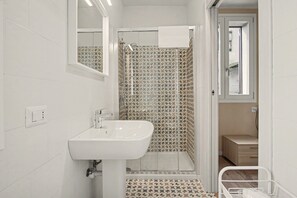 Un bagno con un lavandino bianco, una doccia con piastrelle decorate e una porta che dà su un'altra stanza.