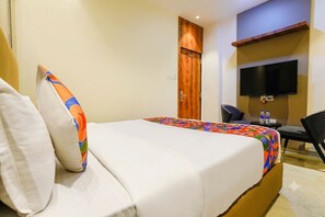 A hotel room with a bed, a television mounted on the wall, a desk with a chair, and a door.