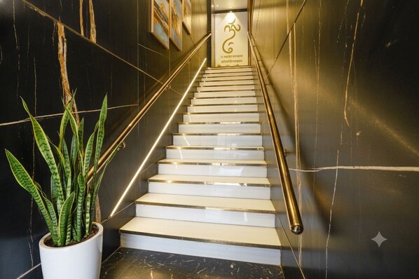 A staircase with white steps and a golden handrail, leading to a landing with a sign.