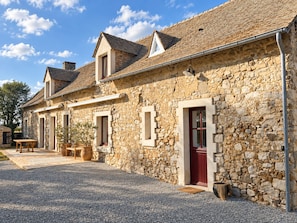 A stone building with a gravel driveway, a wooden table, and a potted plant.