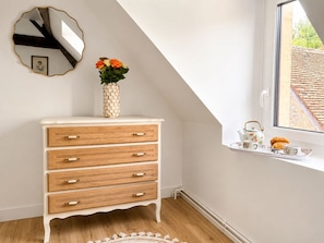 A room with a white dresser, a mirror, a vase with flowers, and a window with a view of a building.