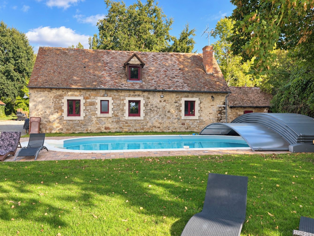 A stone house with a swimming pool, a covered outdoor area, and a lawn with lounge chairs.