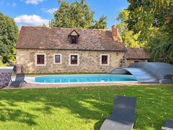 A stone house with a swimming pool, a covered outdoor area, and a lawn with lounge chairs.