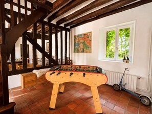 A room with a wooden foosball table, a scooter, a map on the wall, and a window with greenery outside.