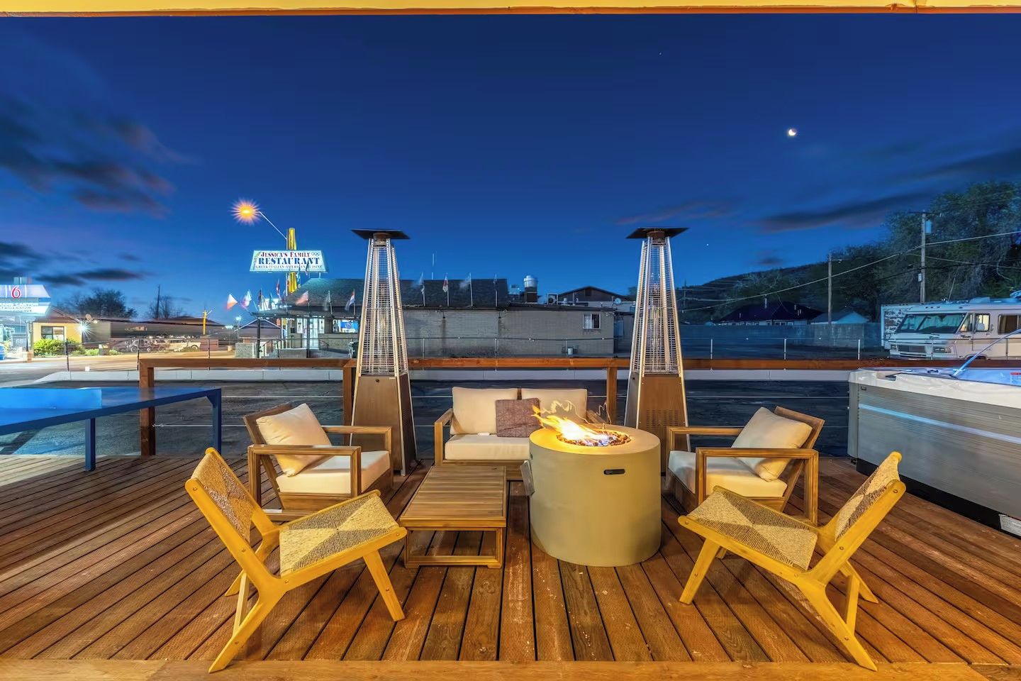 A deck with outdoor seating and a fire feature, overlooking a marina with boats and a restaurant sign.