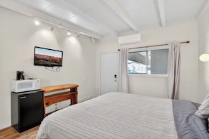Un dormitorio con cama, escritorio con microondas, televisor en la pared y equipo de aire acondicionado.