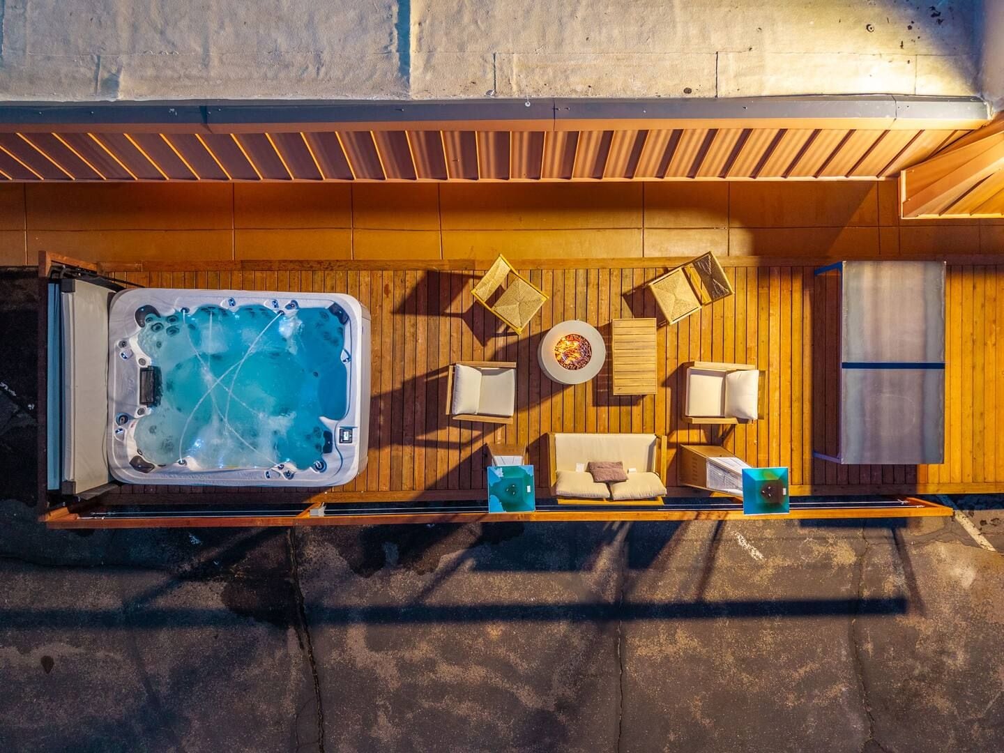 A hot tub with a wooden deck, a lounge chair, a small table, and a wall-mounted heater.