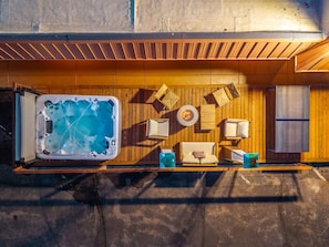 Un jacuzzi con terraza de madera, una silla de descanso, una mesita y un calentador fijado a la pared.