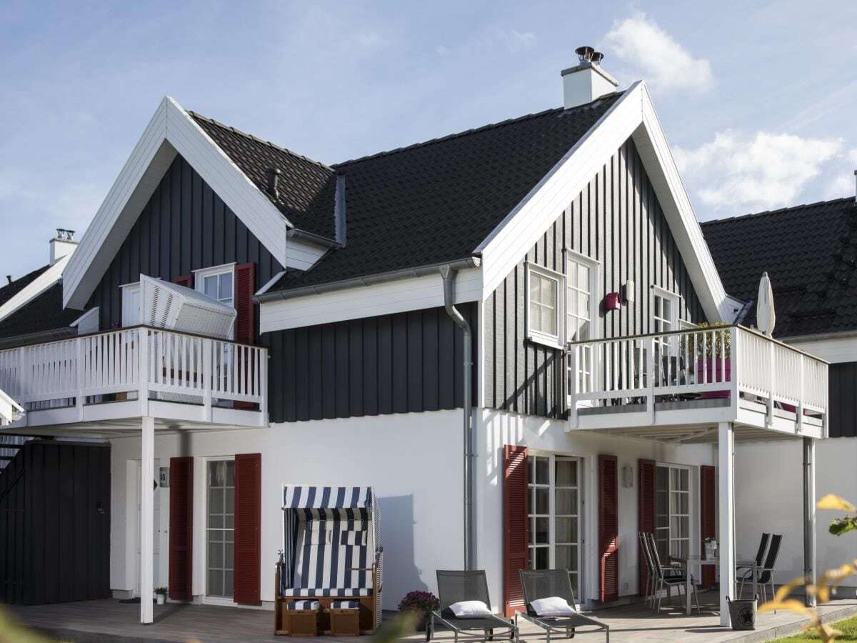 Un bâtiment à deux étages doté d’un balcon, d’un espace extérieur couvert avec des sièges et d’une chaise de plage.