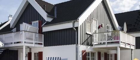 Un bâtiment à deux étages doté d’un balcon, d’un espace extérieur couvert avec des sièges et d’une chaise de plage.