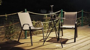 Two chairs and a table on a wooden deck with a rope barrier.