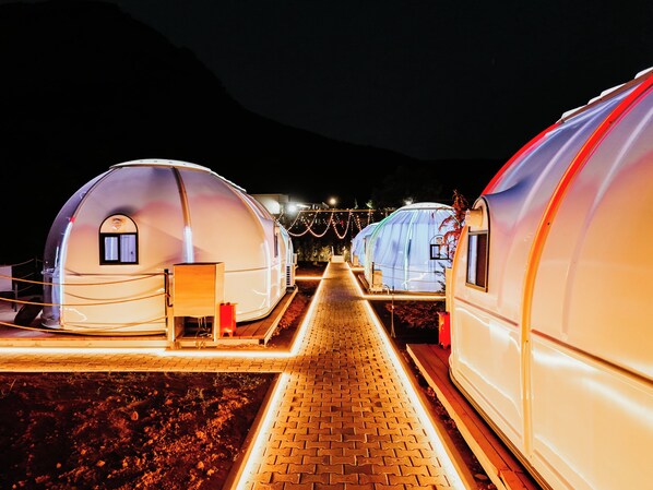 A row of dome-shaped structures with a paved walkway leading to them, each with a small window and a door. - Magas Bubble Houses (Dajt)