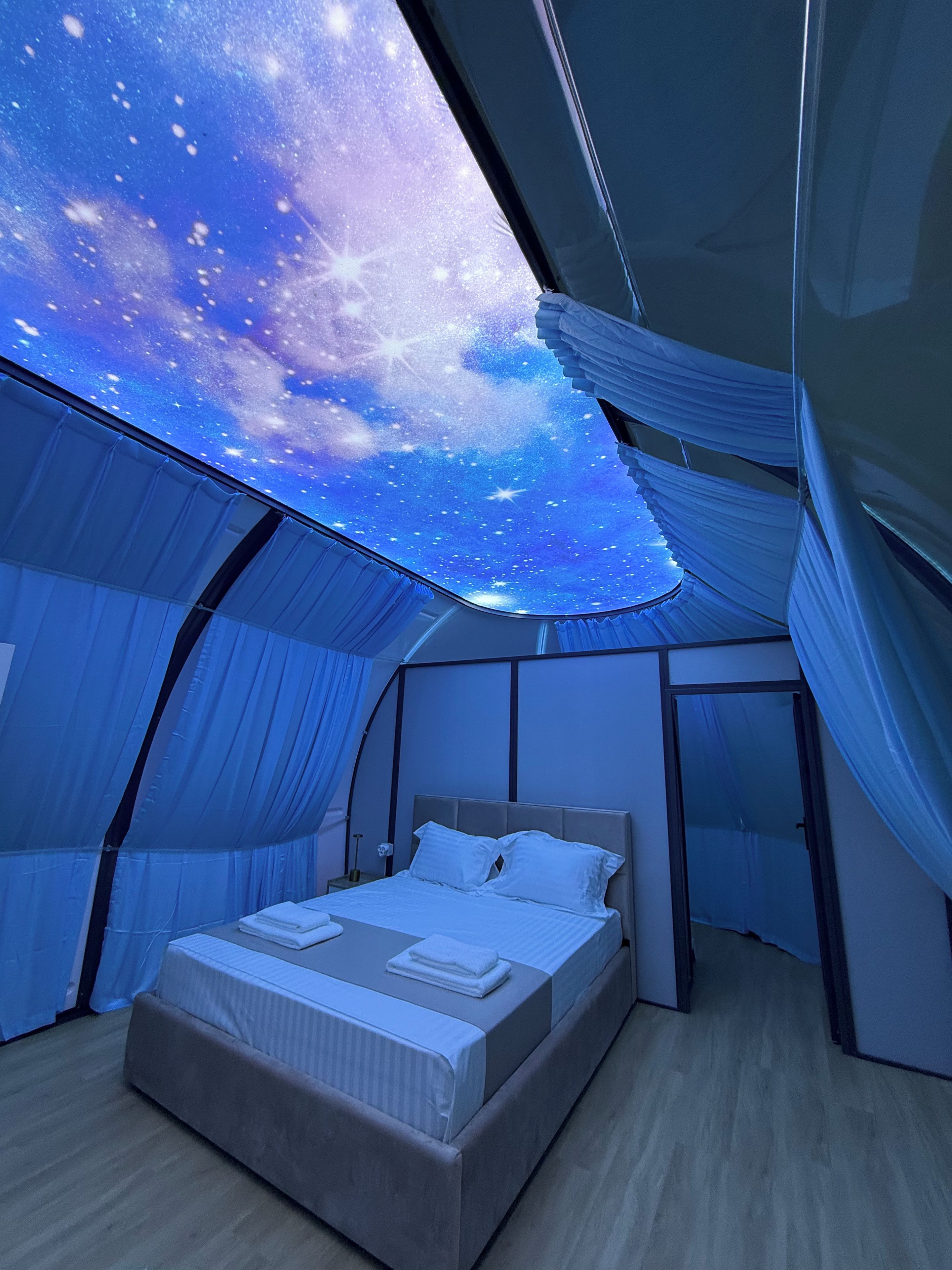 Una habitación con una cama, vistas del cielo a través de una ventana y un techo con diseño de estrellas.