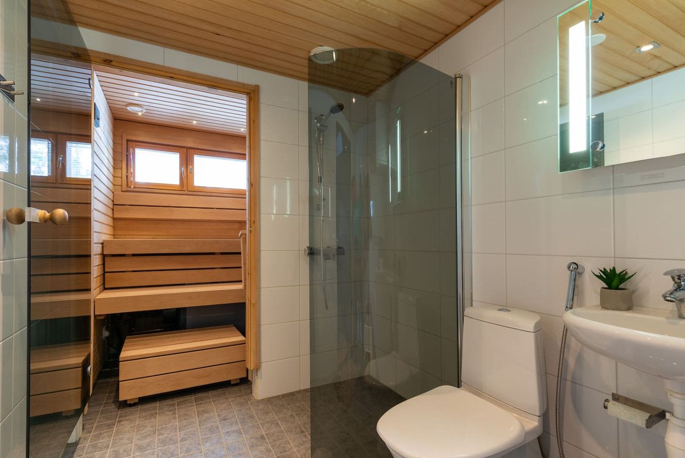 A modern bathroom with a glass-enclosed shower, a wooden bench, and a toilet.