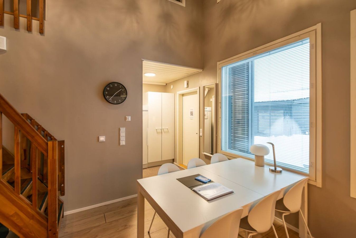 Een modern interieur met een eettafel, stoelen, een klok en een raam met jaloezieën.