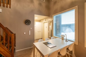 A modern interior with a dining table, chairs, a clock, and a window with blinds.