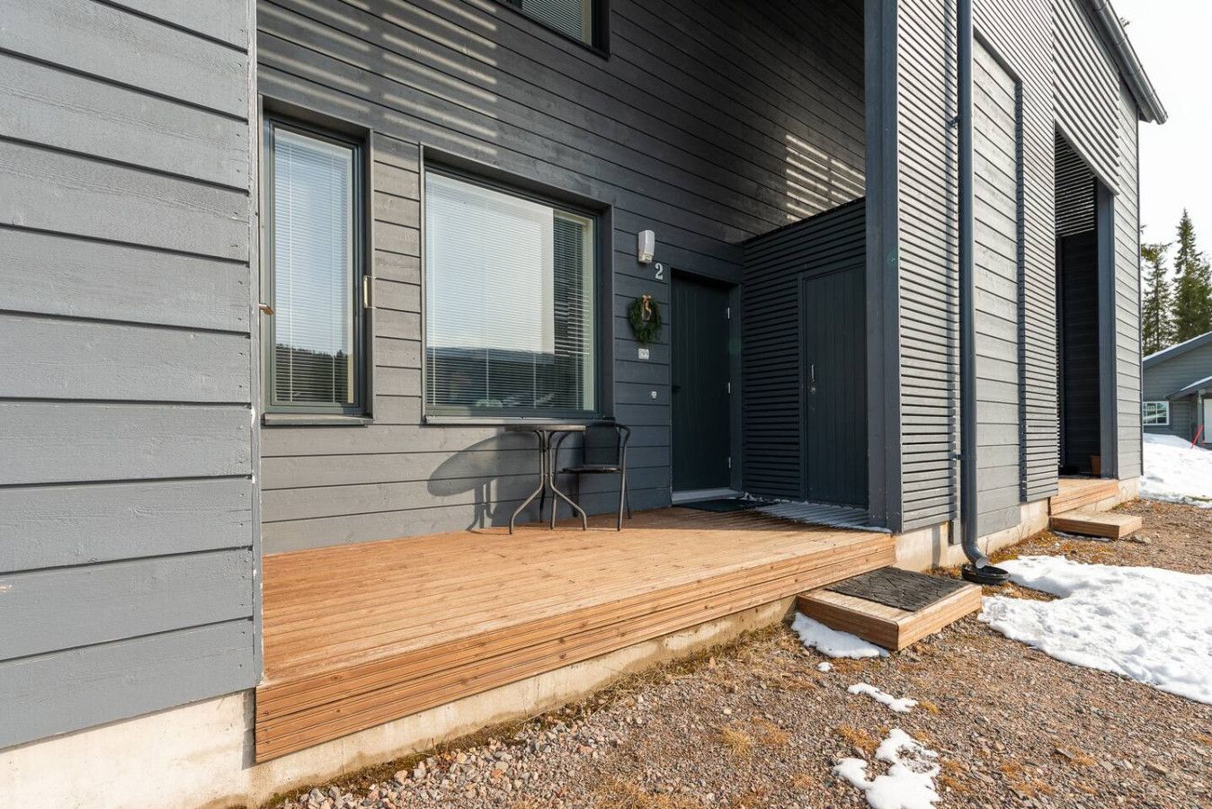 A modern house with a wooden deck, a covered porch, and a garage door.