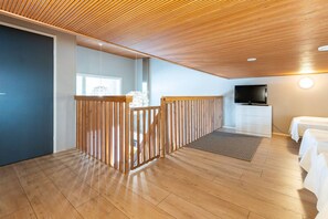A room with a wooden ceiling, a TV, a bed, and a white dresser.