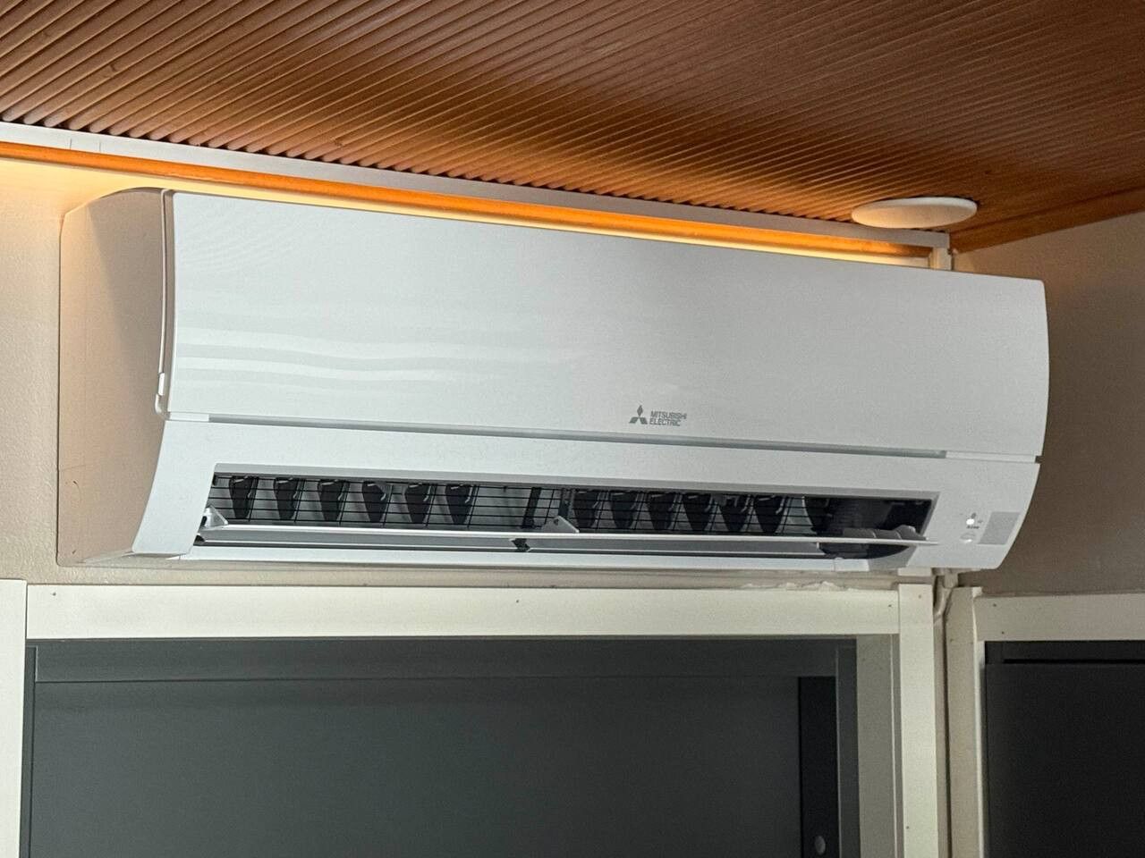 En Mitsubishi aircondition-enhed monteret på en væg med et træloft over.