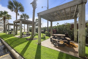 Outdoor wooden structures with picnic tables, surrounded by well-maintained grass and palm trees. - Cute condo on Seawall across from beach (Galveston)