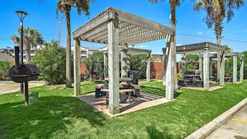 A gazebo with a grill and picnic tables in a well-maintained grassy area.