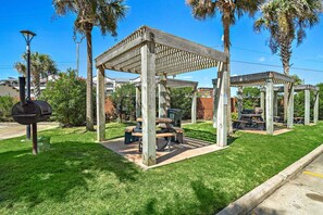Un jardín techado con una parrilla y mesas de picnic en un césped cuidado.