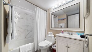 Et badeværelse med badekar, toilet, vask og et spejl med lys over.