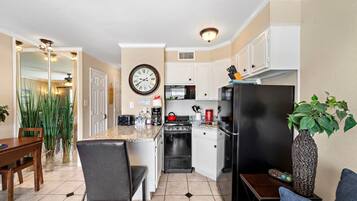 A compact kitchen with a dining area, a clock on the wall, and a plant on the counter.